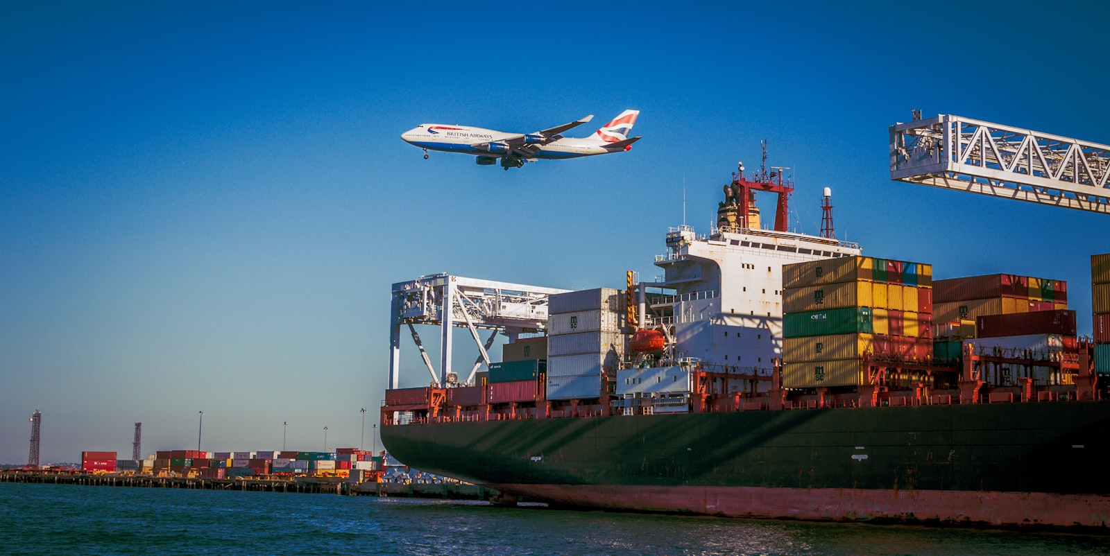 airplane on mid air passing by above cargo ship